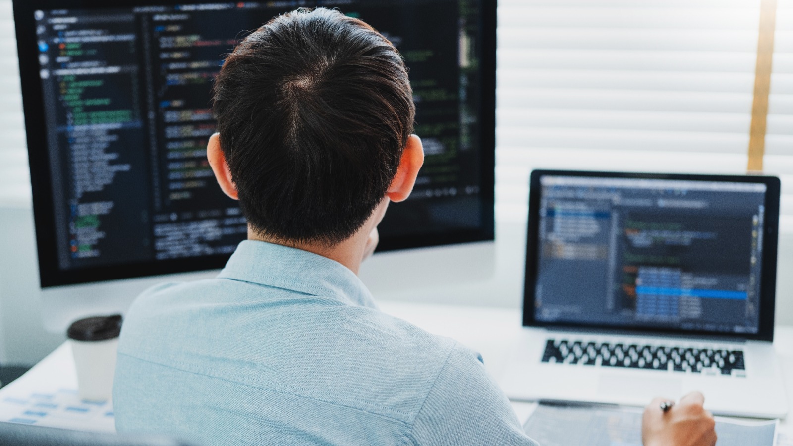 パソコンのモニターを見ながらメモを取る男性