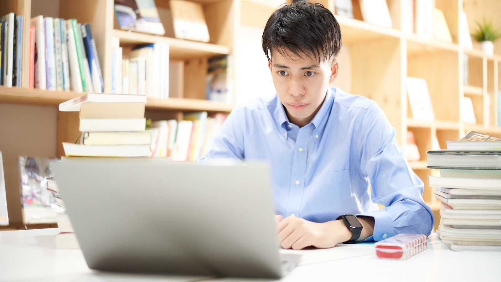 本を積み真剣な表情でパソコンの見る男性
