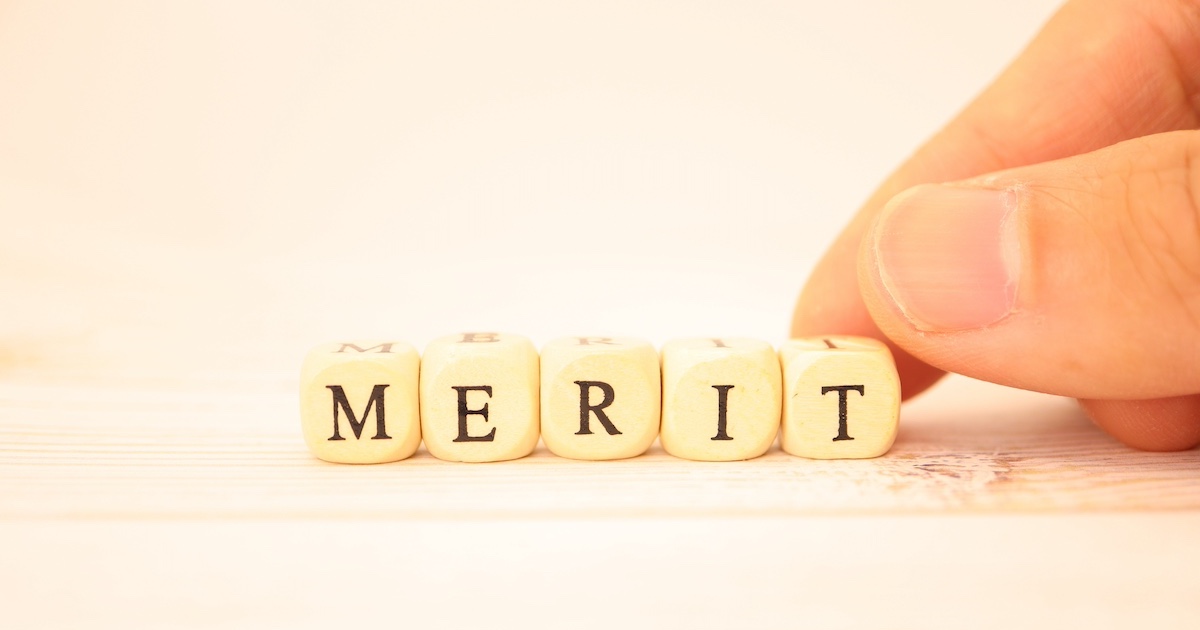 「MERIT」と書かれた小さなキューブとそれをつまむ指