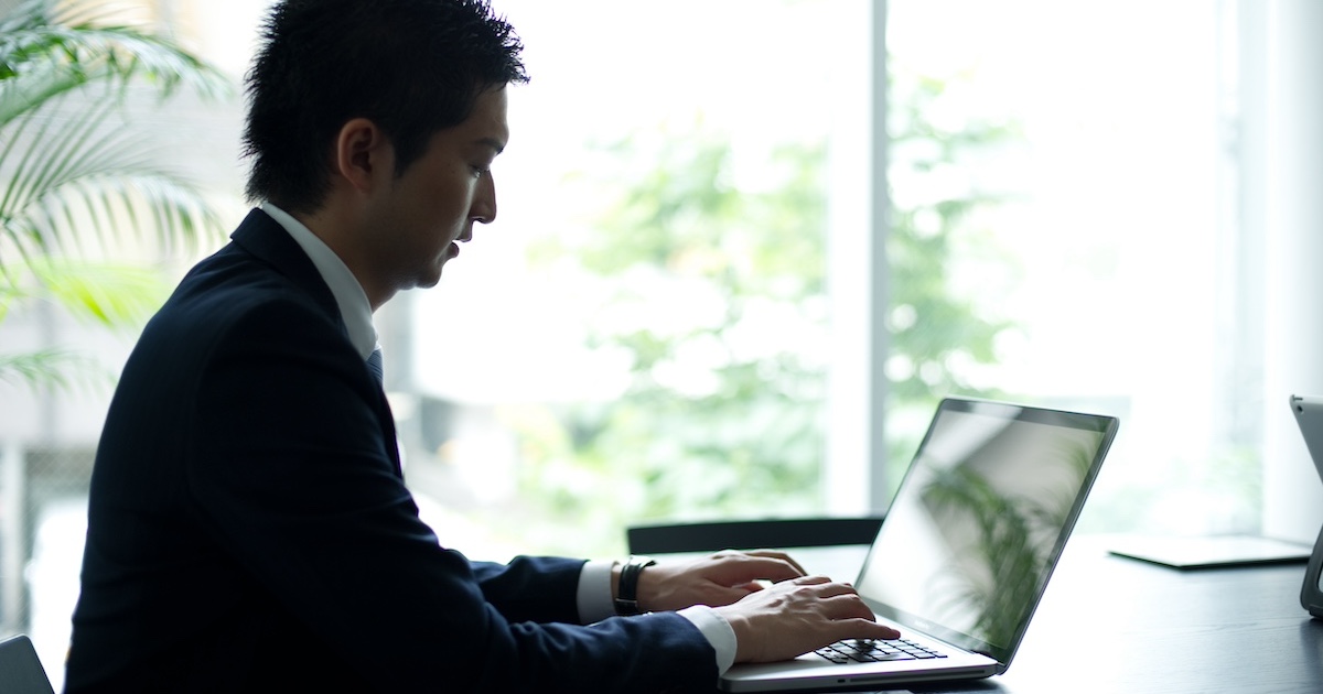 窓際でパソコンで仕事をするビジネスパーソン