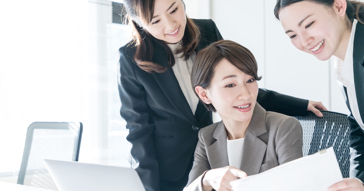 3人のビジネスパーソンが資料を手に話す様子