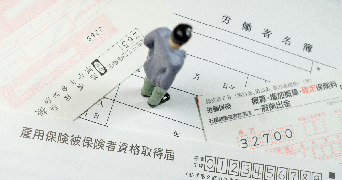 労働保険に関する書類の上に立っている男性の人形