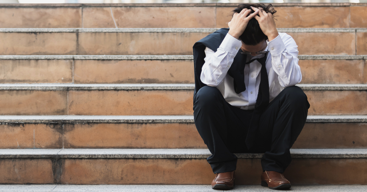 階段に座り込み、頭を抱えるスーツ姿の男性