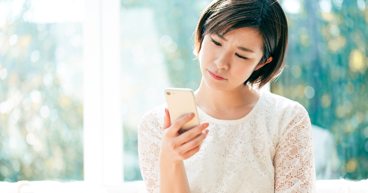 困った表情でスマホを見つめる女性