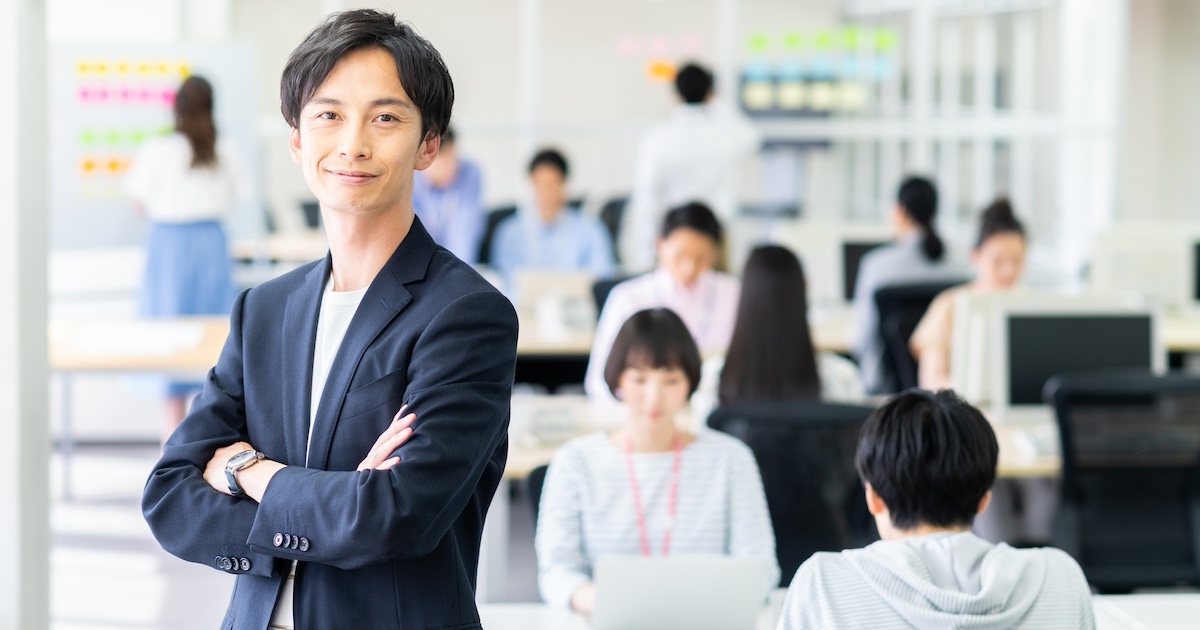 ビジネスのフロアで腕を組み微笑むビジネスパーソン