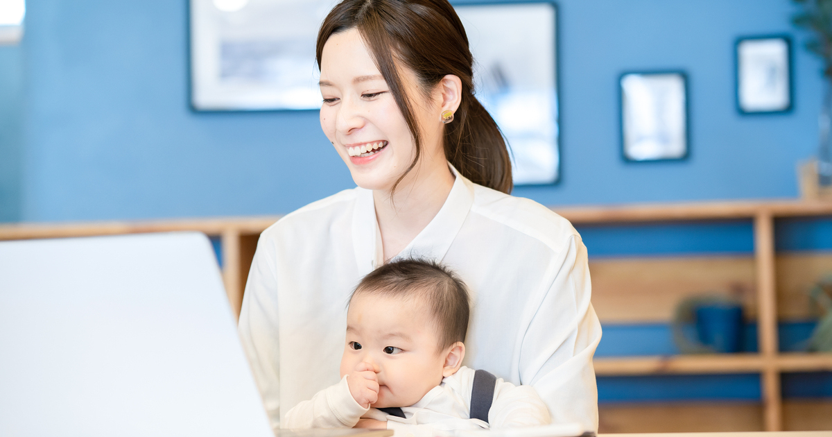赤ちゃんを抱きながらパソコン作業をする笑顔の妊婦