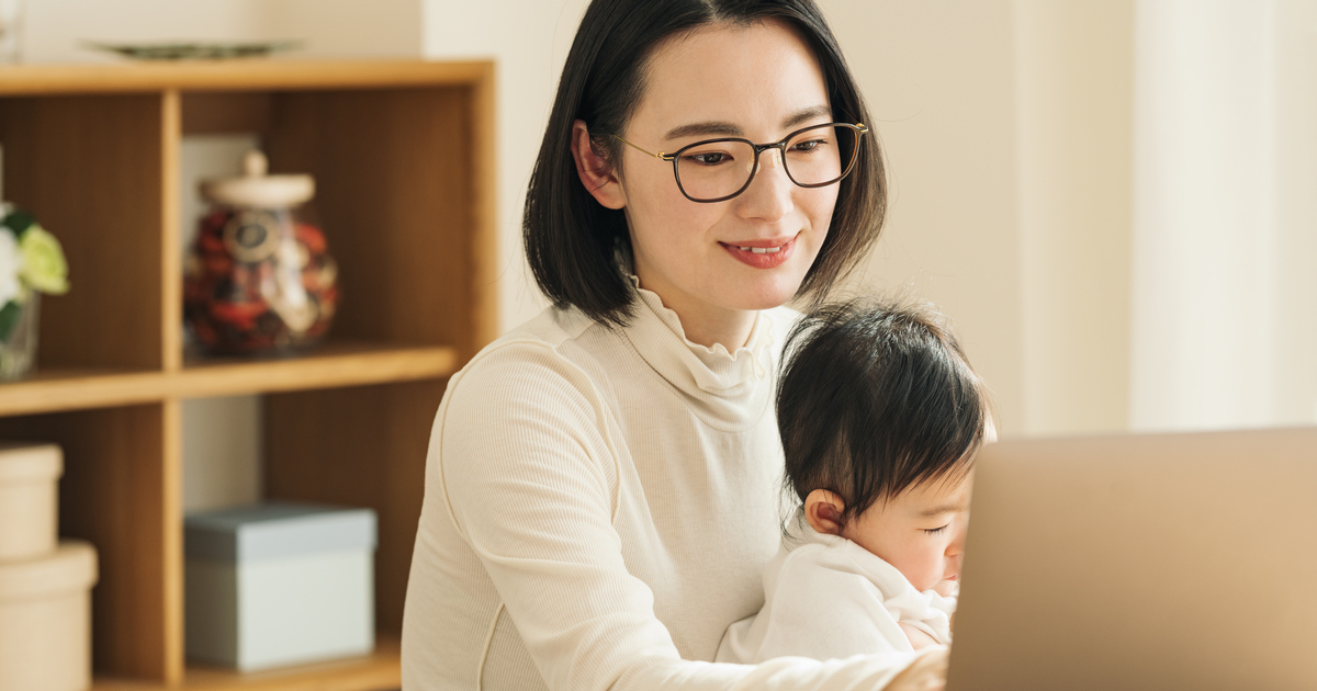 赤ちゃんを抱きながらパソコン作業をする笑顔の妊婦