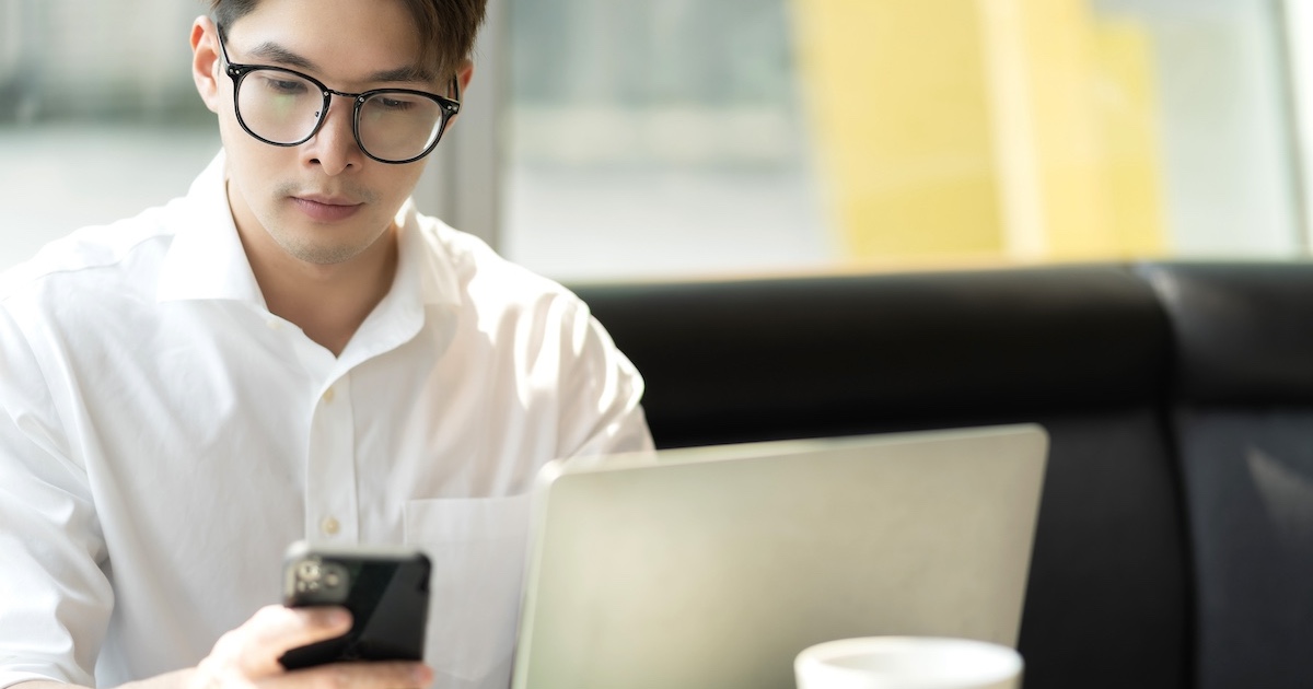 スマホを手にしながらパソコンも広げ作業する男性