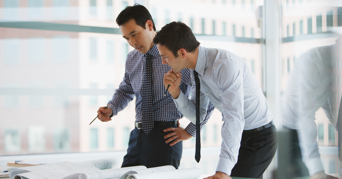 机に資料を置き、立ったまま話し合うビジネスパーソン