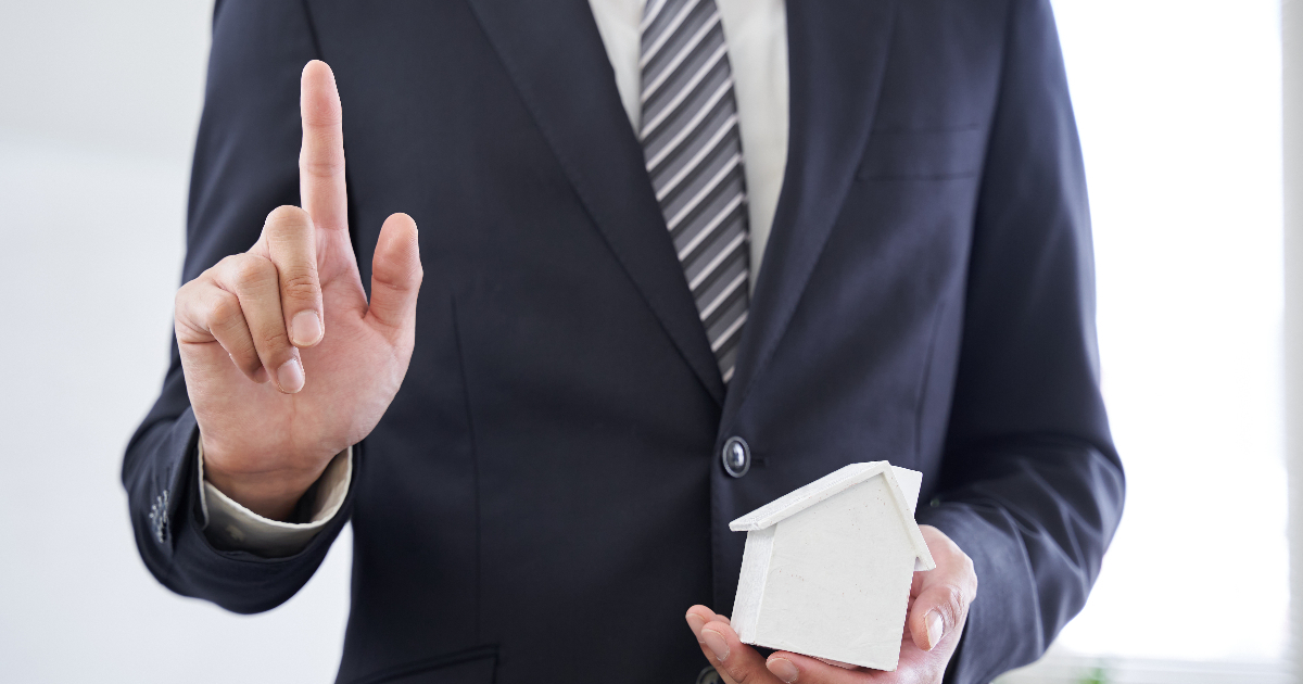 家の模型を持ちながら指をさす男性