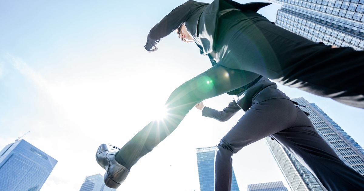 ビジネス街をジャンプしながら進むビジネスパーソン