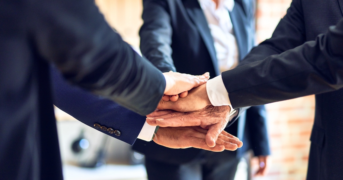 オフィスで手を合わせて円になって立っているビジネスパーソン達