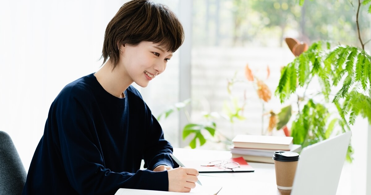 パソコンの前で手帳を書いている女性