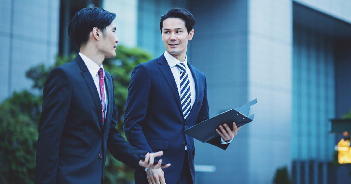 外で会話しながら歩くスーツを着た2人の男性