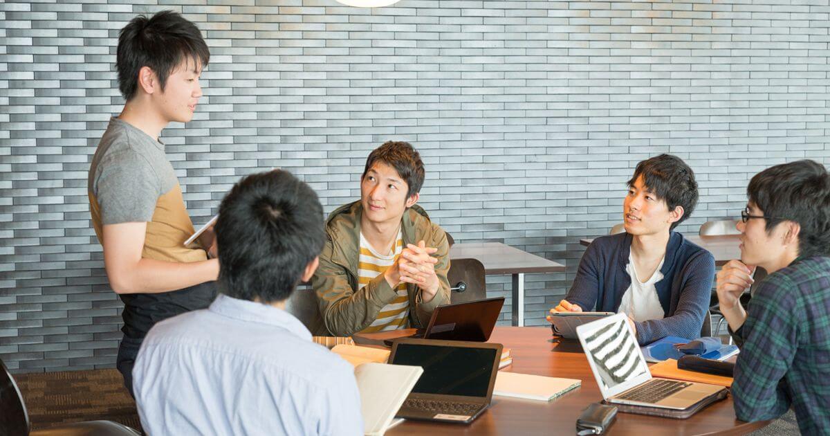 机でパソコンを開きながら対話する5人の男性