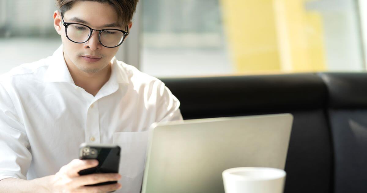 パソコンの前でスマートフォンを操作する眼鏡をかけた男性