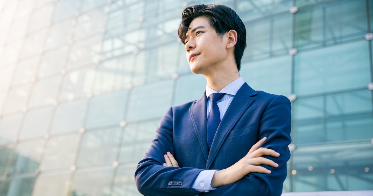 ビルの前で腕を組み遠くをみつめるビジネスパーソン