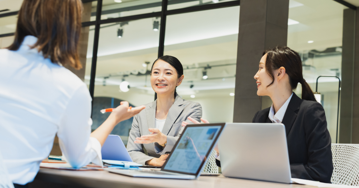 ミーティング中の3人の女性社員、デスクにパソコンが置いてある