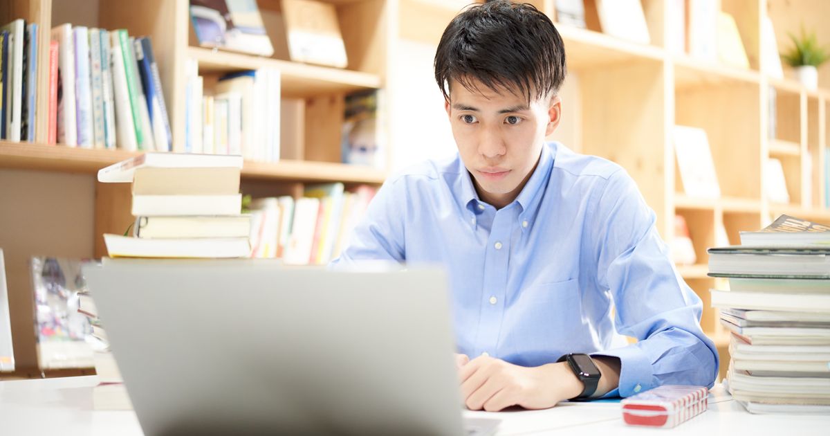 本棚の前のデスクでノートパソコンを使う男性