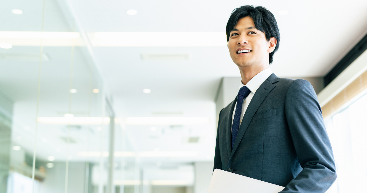 ノートを手に持つ、笑顔のスーツ姿の男性