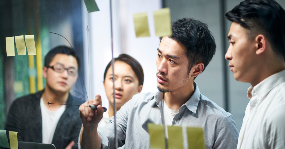 ガラスボードに図を描きながら、数人のメンバーと議論しているビジネスチーム