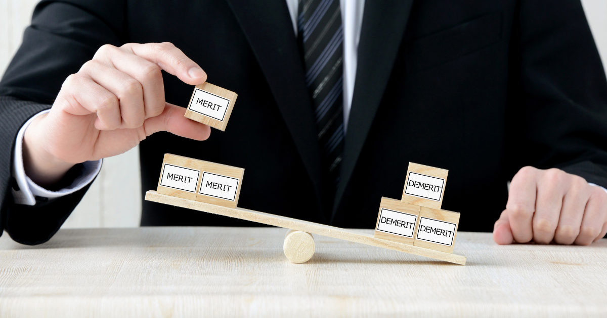 メリットとデメリットのブロックをシーソーに乗せているビジネスパーソンの手元