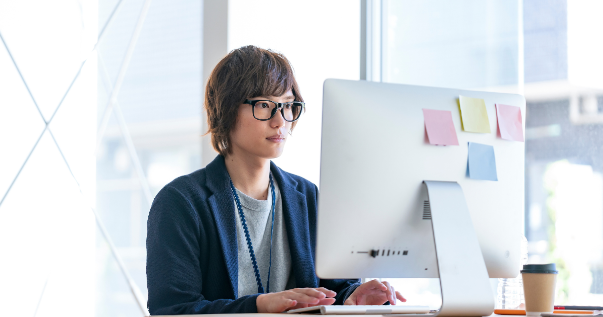 オフィスでパソコンを使う眼鏡をかけた男性、モニター背面に4枚の付箋が貼ってある