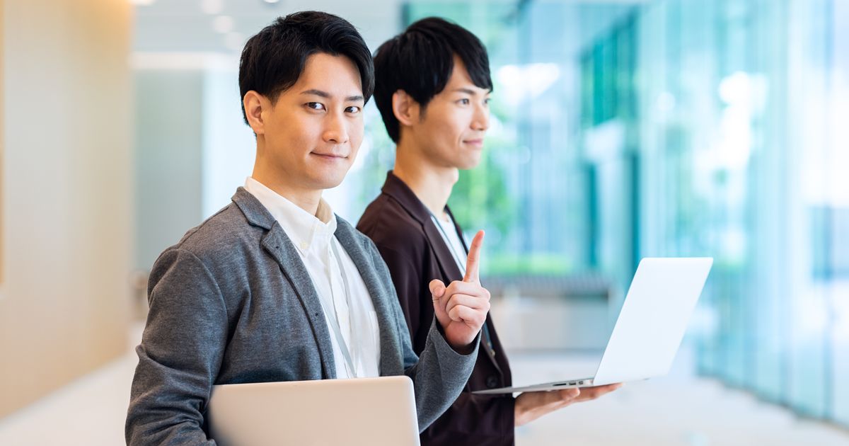 ノートPCを持ち、指差しポーズをするアジア人ビジネスマン2人