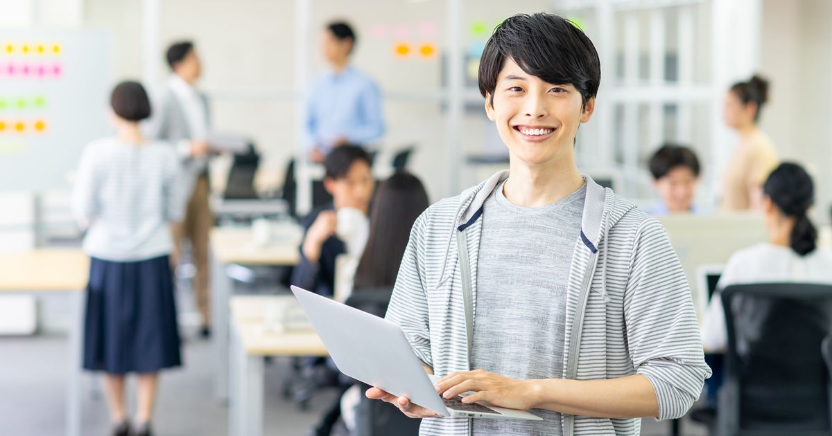 オフィスでノートパソコンを抱え笑顔で立つ男性