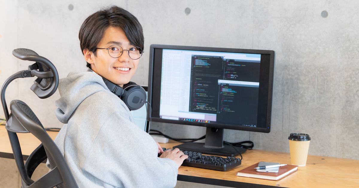 ヘッドホンを首にかけ、モニターに向かって笑顔で作業する男性