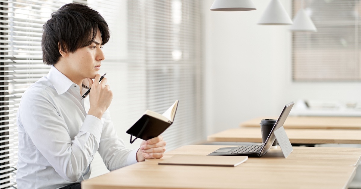 手帳を手に、PCを見つめ考える男性
