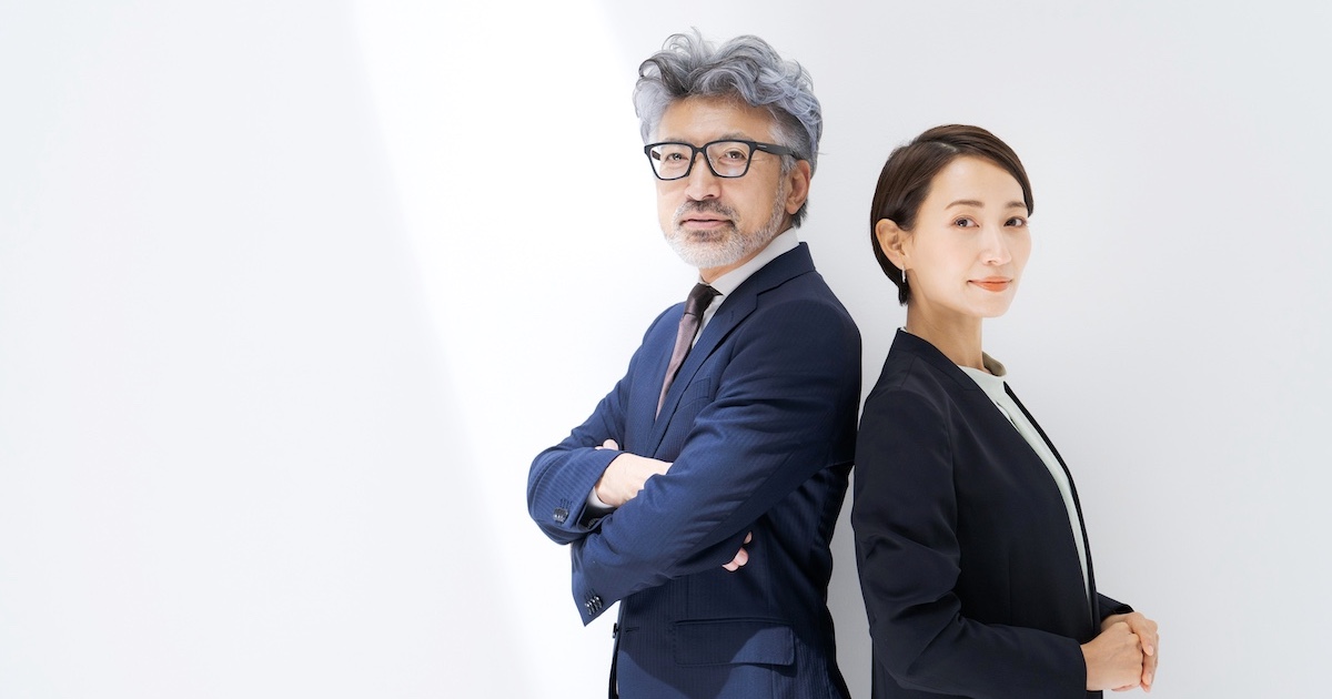 背中合わせになりこちらを見つめる男女のビジネスパーソン2人