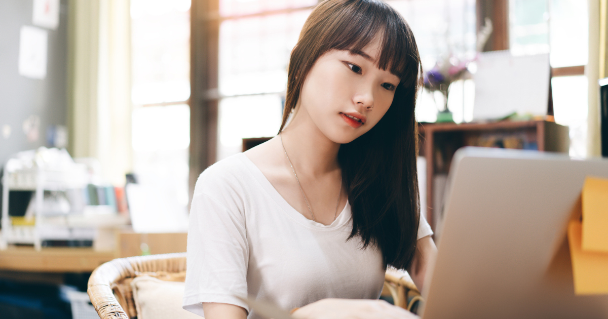 室内で、白いTシャツを着た若い女性がノートパソコンで作業している様子