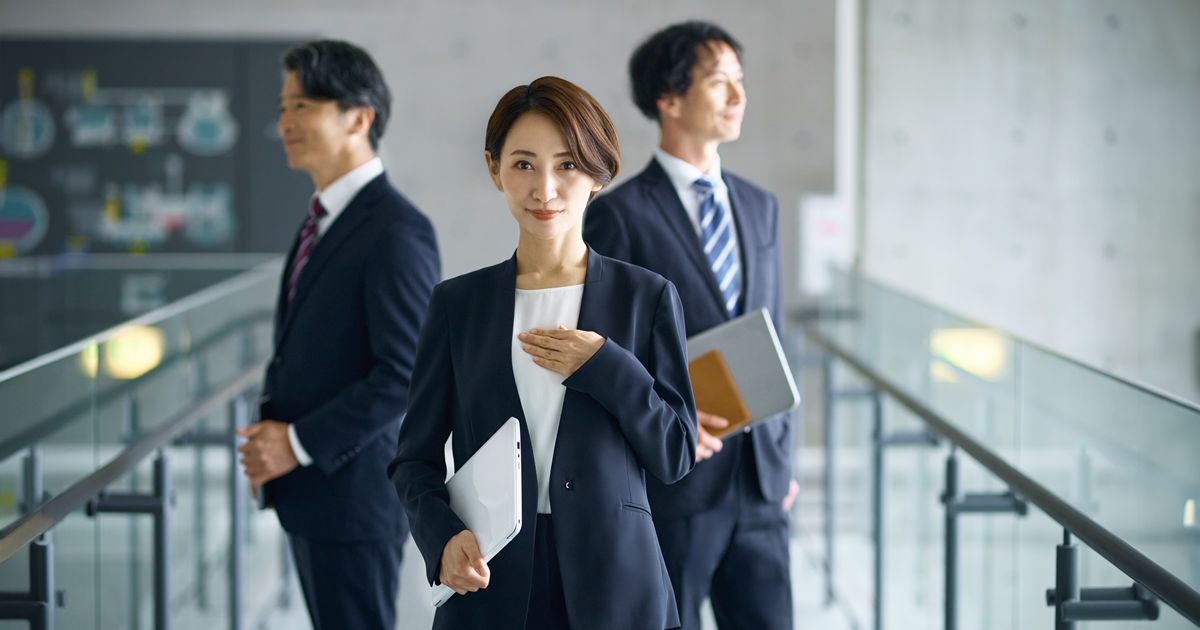 ノートパソコンを抱え胸に手を当てる女性と後ろに立つビジネスマン