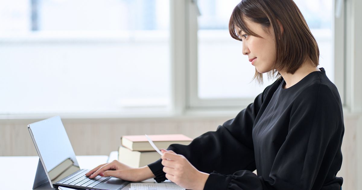 領収書を手に持ちノートパソコンで作業をする女性