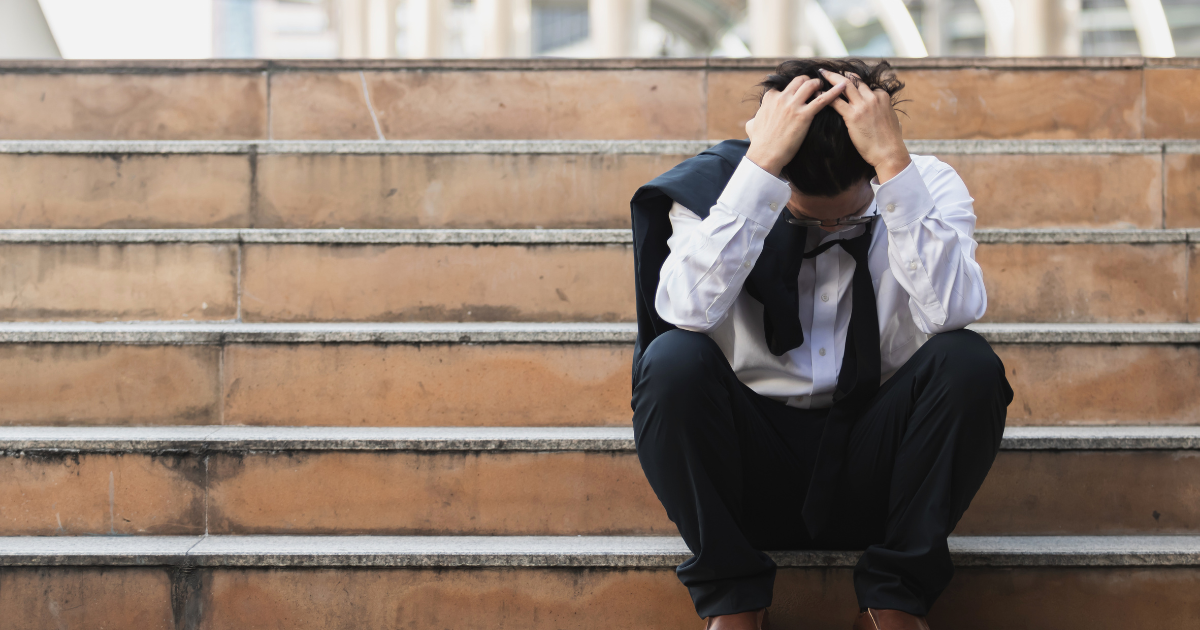 階段に座り込み、頭を抱えて悩んでいるスーツ姿の男性
