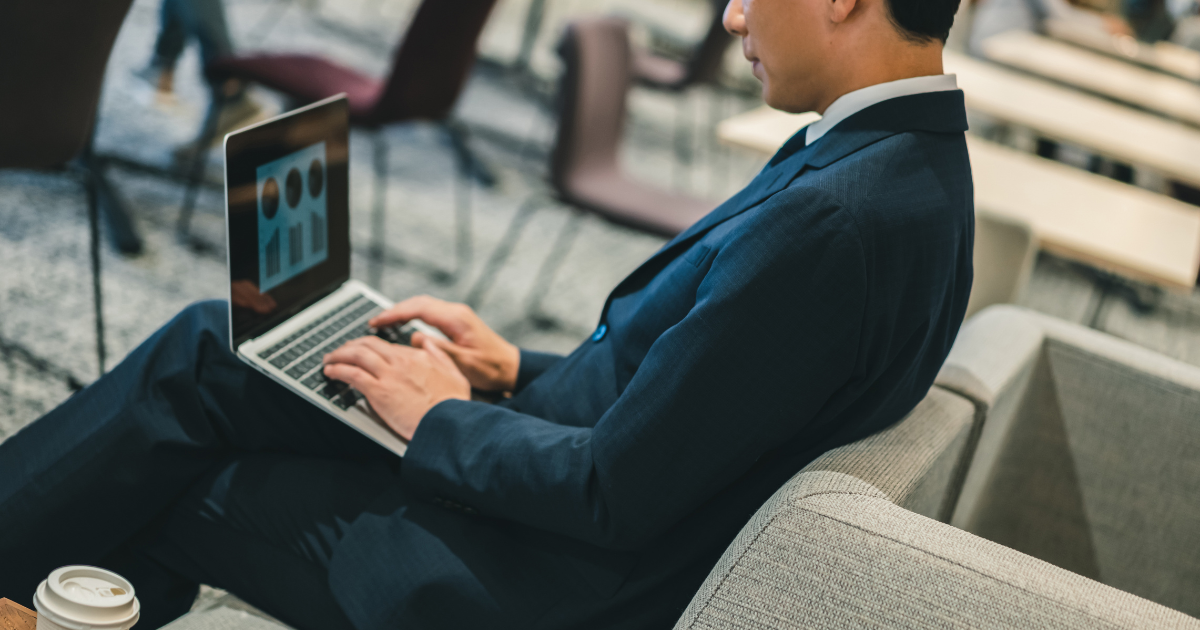 待合室でパソコンを操作しているスーツ姿の男性を横から写した姿