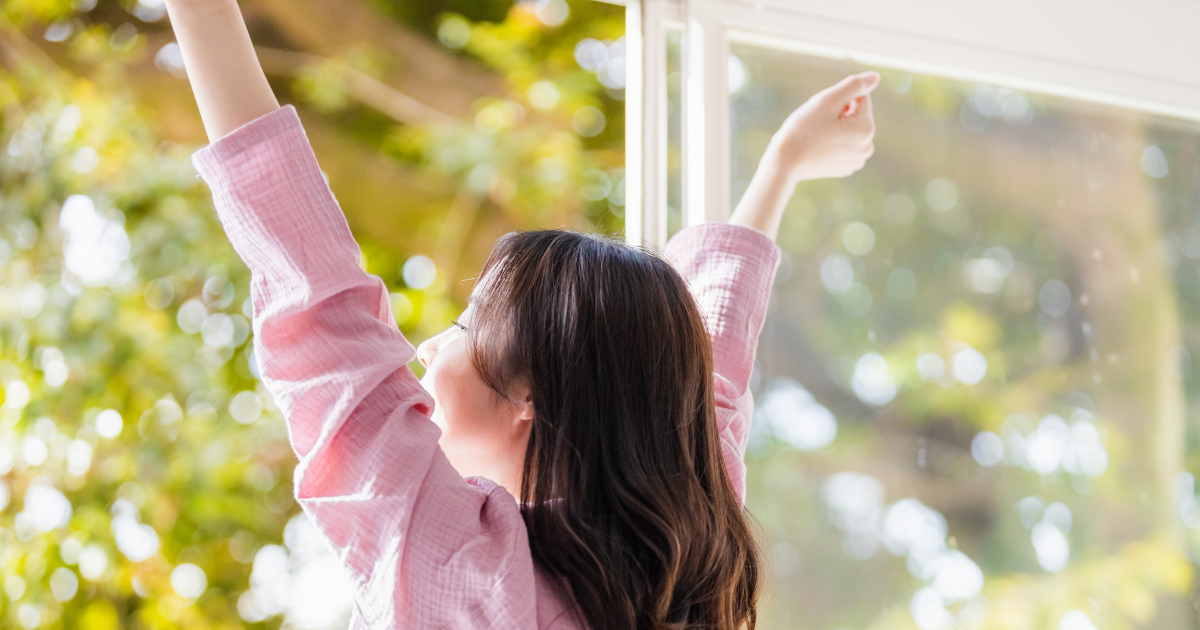 朝に窓辺で軽く体を伸ばして目覚める女性