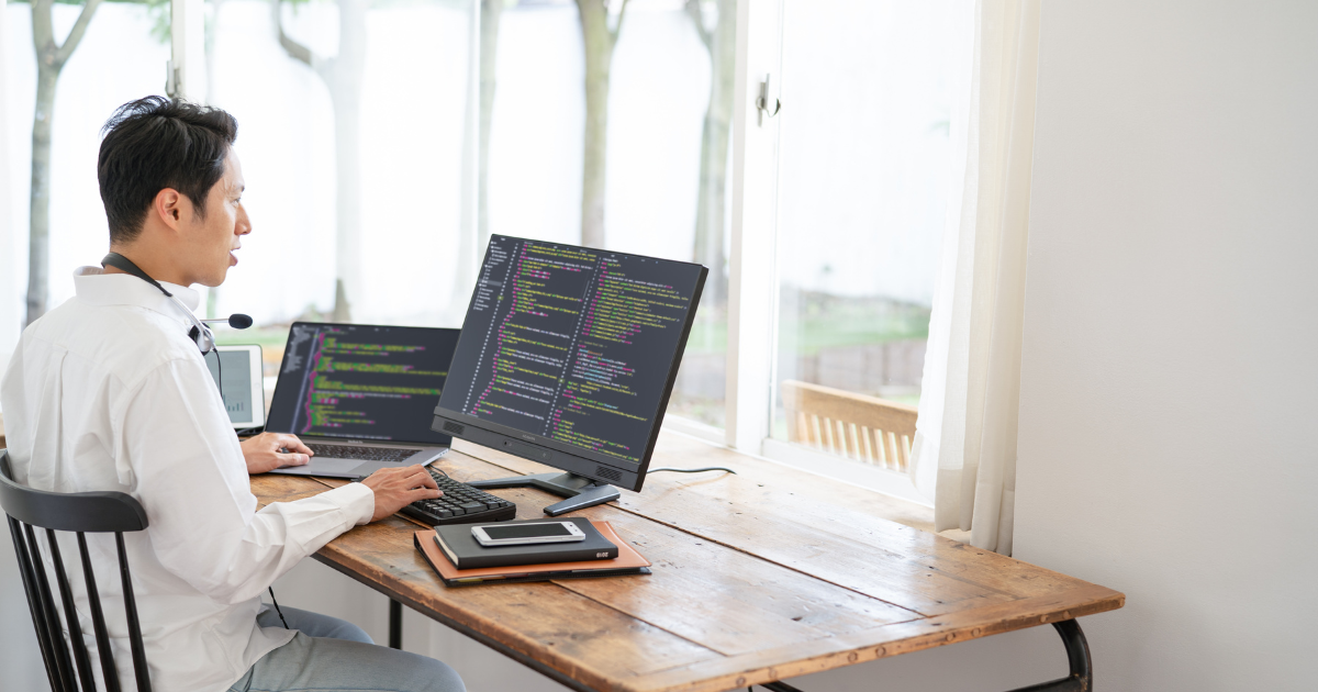 デスクでPC作業をする在宅ワーカー、画面にプログラムコードが表示されている