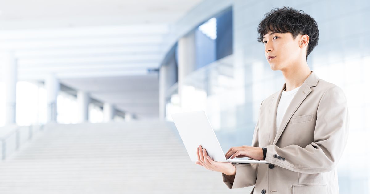 近代的なオフィスビルでノートパソコンを開き佇む男性