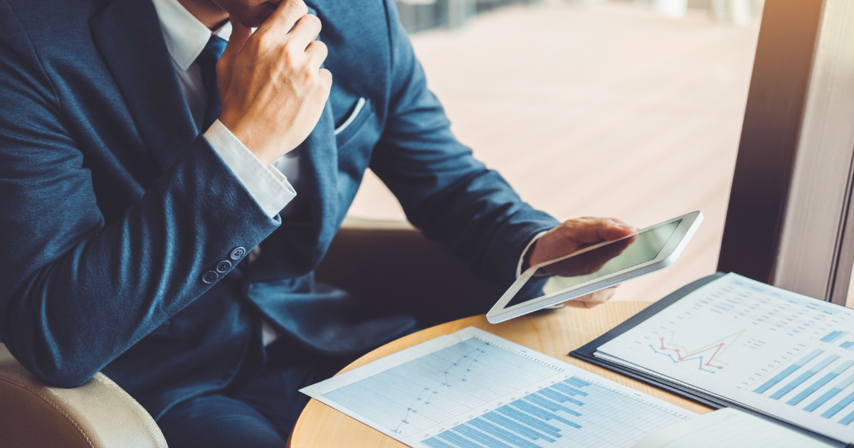 スマホを片手に持ち顎に手を当てて考える雰囲気の男性、丸テーブルの上に書類が置いてある