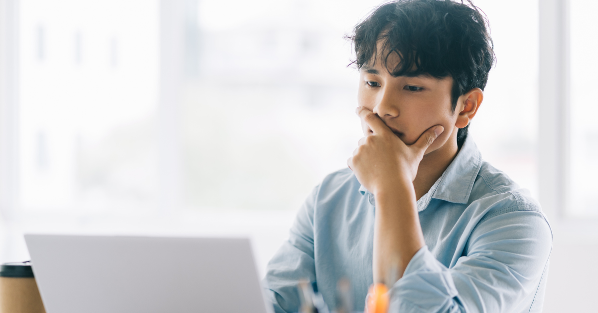 ノートPCの前で考え込み、作業が進まず手が止まる男性