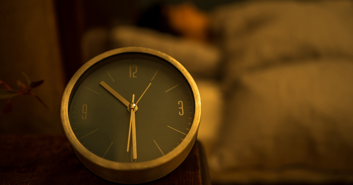ベッドサイドに置かれた目覚まし時計と睡眠を確保する人