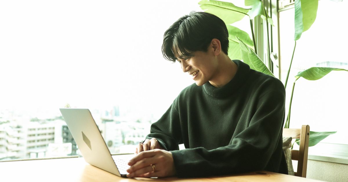 窓際でノートパソコンを見て微笑む男性
