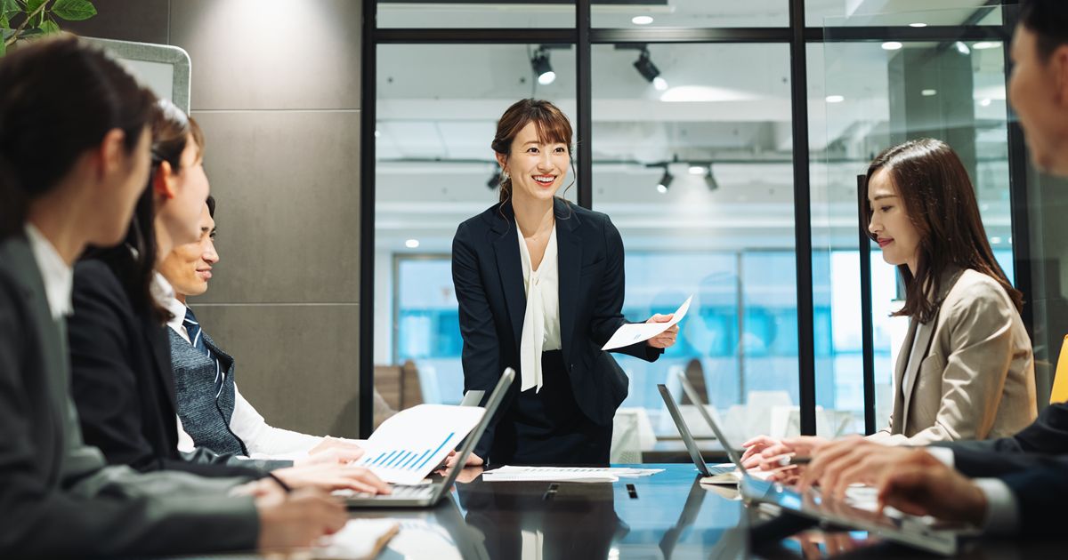会議室で資料を持ち笑顔で進行する女性リーダーと参加者