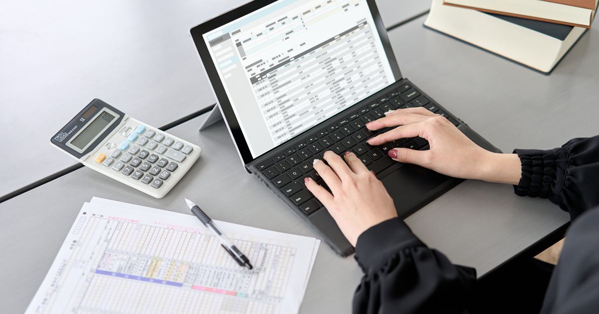 確定申告の書類を横に置いてノートパソコンを操作する人