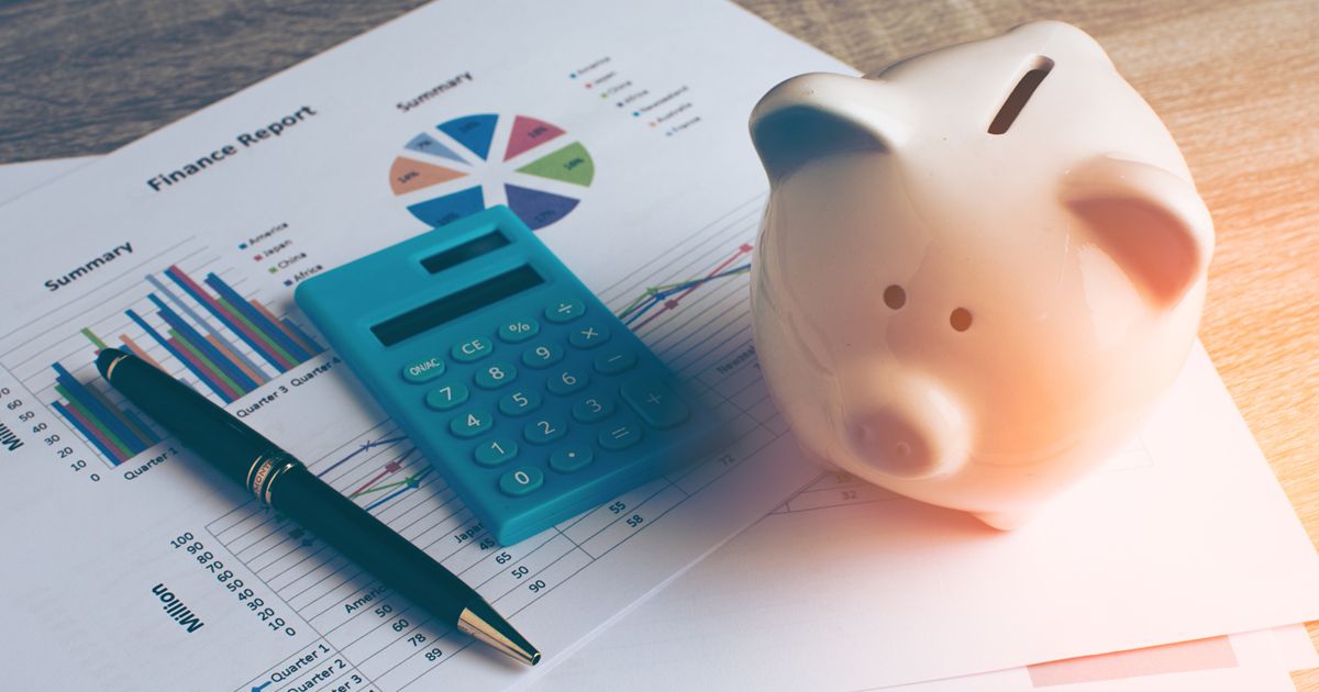 グラフが描かれた資料の上に置かれた豚の貯金箱と電卓