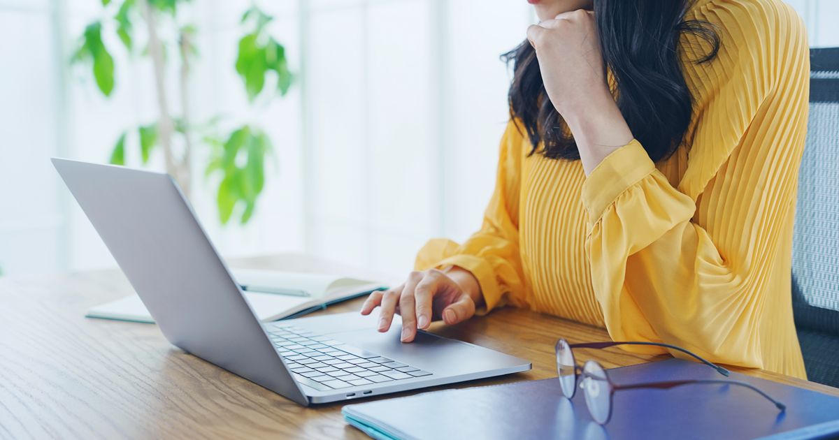 デスクでノートパソコンを操作する黄色い服の女性