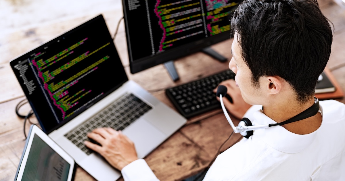 ヘッドホンを首にかけPCで作業する男性