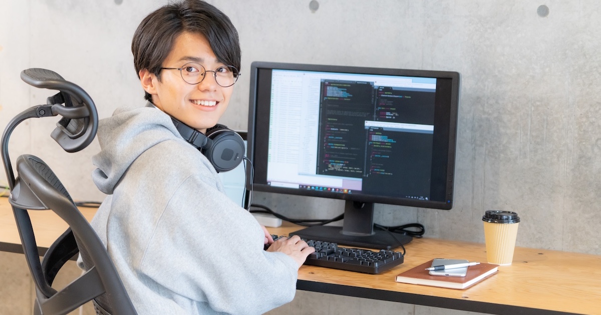 ヘッドホンを首にかけパソコン作業中にこちらを振り向く男性